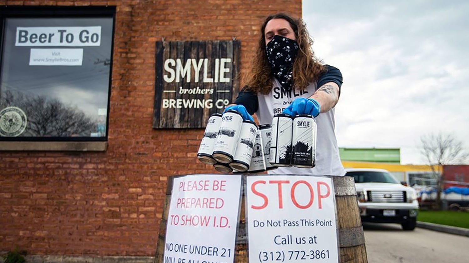 A brewer from Smylie outdoor, wearing a mask and gloves, dropping a beer order onto a to-go pickup station