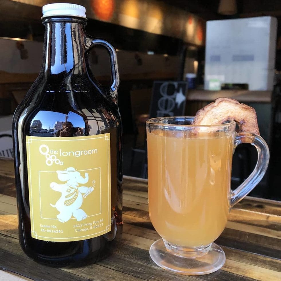 A growler of Toddy Appleseed next to a glass served warm with an apple chip garnish
